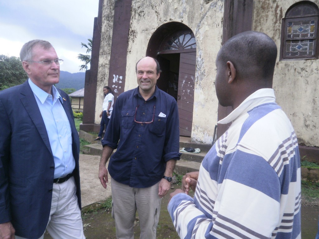 Singhammer(L) listens to the Rev.Fr Emmanuel Epie(R) Parish Priest of the oldest Catholic Church in English speaking Cameroon(in the background) built by the German Palotine Missionaries in 1896